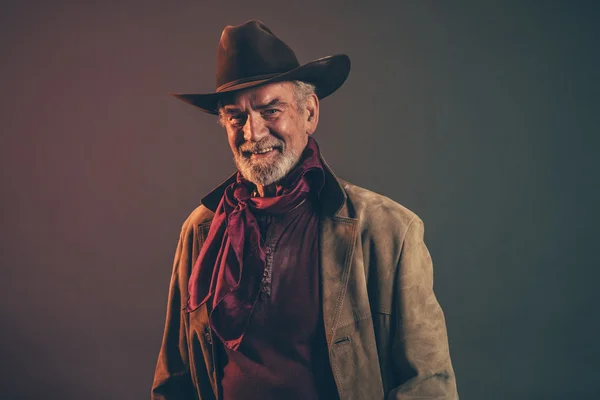 Lachende oude ruwe westerse cowboy met grijze baard en bruin hoed. — Stockfoto