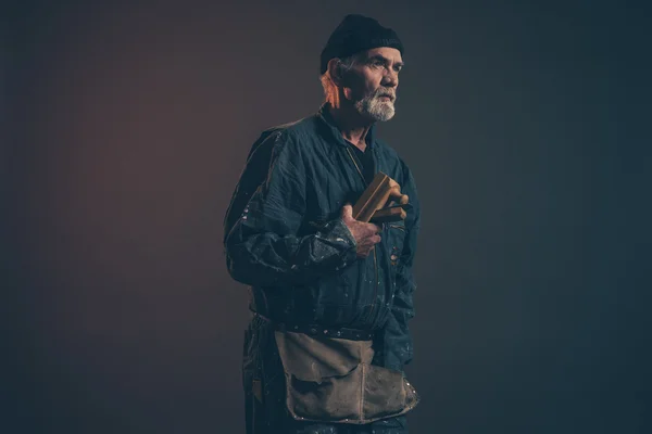 Senior carpenter with gray hair and beard holding old plane wear — Stock Photo, Image