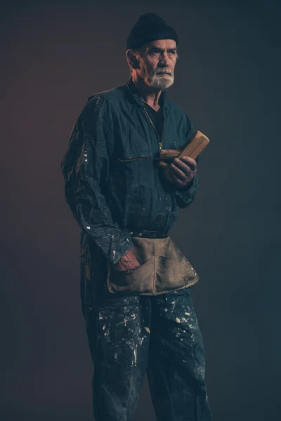 Senior timmerman met grijs haar en baard houden oude vliegtuig slijtage — Stockfoto