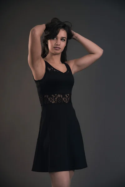 Cute brunette teenage girl with hands in hair wearing black dres — Stock Photo, Image