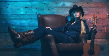 Akustik gitar ile cowgirl country şarkıcısı. Deri üzerinde oturan 