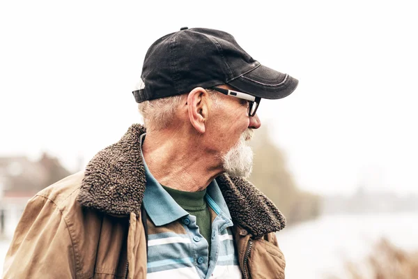 Uomo anziano con barba indossa occhiali e berretto nero all'aperto in w — Foto Stock