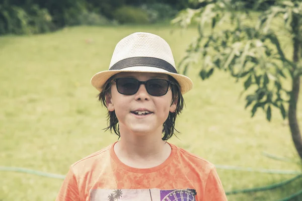 Teenage sommaren pojke med hatt och solglasögon i trädgården. — Stockfoto