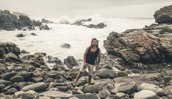 Man with long blonde hair standing on rocky shore at Tsitsikamma — Stock Photo, Image