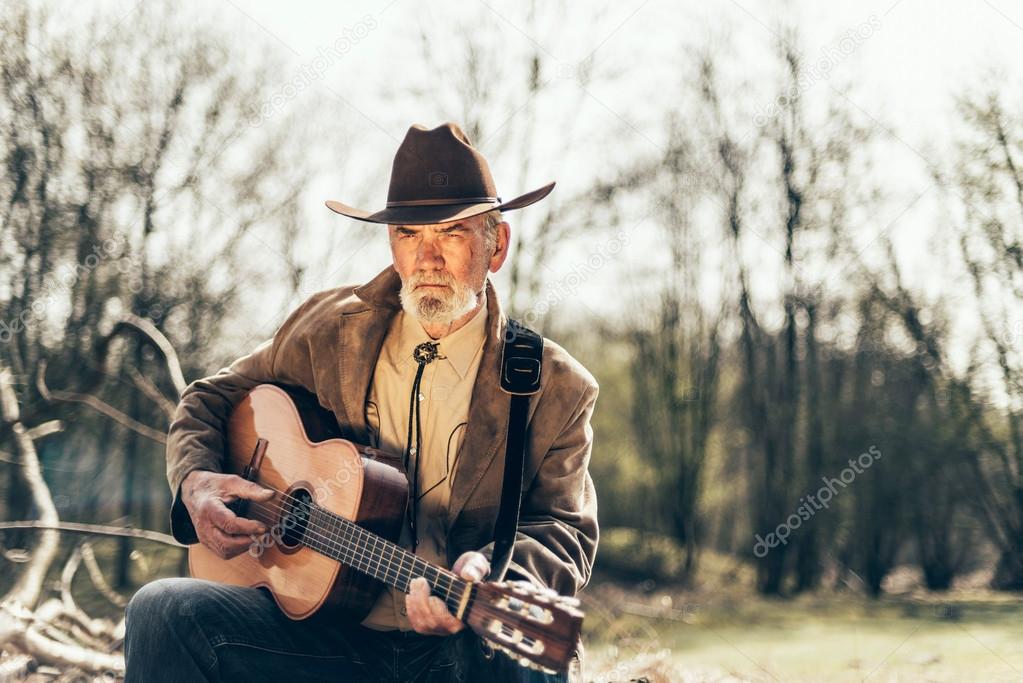 Elderly musician sitting strumming a guitar