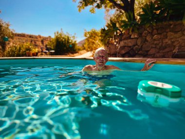 Senior man in swimming pool in garden on a sunny day. Andalucia, Spain.