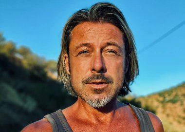 Orta yaşlı, bronz tenli, yarı sarı saçlı, gri sakallı, atlet gömlekli, altın saatinde dışarıda yürüyen bir adam. Almogia tepeleri, Malaga, Endülüs, İspanya.