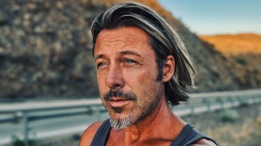 Orta yaşlı, bronz tenli, yarı sarı saçlı, gri sakallı, atlet gömlekli, altın saatinde dışarıda yürüyen bir adam. Almogia tepeleri, Malaga, Endülüs, İspanya.