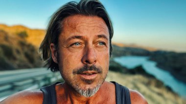 Orta yaşlı, bronz tenli, yarı sarı saçlı, gri sakallı, atlet gömlekli, altın saatinde dışarıda yürüyen bir adam. Almogia tepeleri, Malaga, Endülüs, İspanya.