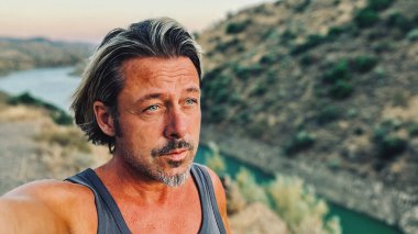 Orta yaşlı, bronz tenli, yarı sarı saçlı, gri sakallı, atlet gömlekli, altın saatinde dışarıda yürüyen bir adam. Almogia tepeleri, Malaga, Endülüs, İspanya.