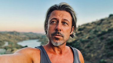 Orta yaşlı, bronz tenli, yarı sarı saçlı, gri sakallı, atlet gömlekli, altın saatinde dışarıda yürüyen bir adam. Almogia tepeleri, Malaga, Endülüs, İspanya.