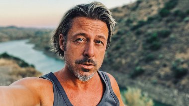 Orta yaşlı, bronz tenli, yarı sarı saçlı, gri sakallı, atlet gömlekli, altın saatinde dışarıda yürüyen bir adam. Almogia tepeleri, Malaga, Endülüs, İspanya.