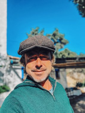 Yünlü gazeteci şapkası ve sakallı, yeşil yünlü süveteri olan, neşeli, haşin bir adam..