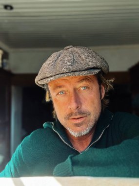 Yünlü gazeteci şapkası ve sakallı, yeşil yünlü süveteri olan haşin bir adam..