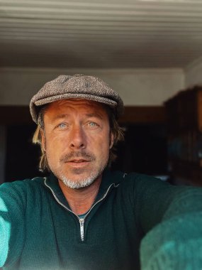 Yünlü gazeteci şapkası ve sakallı, yeşil yünlü süveteri olan haşin bir adam..