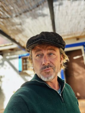 Yünlü gazeteci şapkası ve sakallı, dışarıda verandanın altında yünlü süveter giyen etkileyici, haşin bir adam..