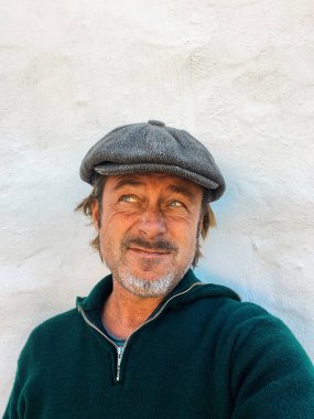 Yünlü gazeteci şapkası ve sakallı, yeşil yünlü süveteri olan etkileyici, haşin bir adam. İspanyol evinin beyaz duvarının yanında..