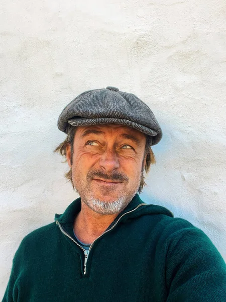 Yünlü gazeteci şapkası ve sakallı, yeşil yünlü süveteri olan etkileyici, haşin bir adam. İspanyol evinin beyaz duvarının yanında..