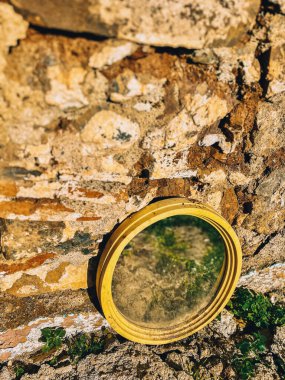 Eski oval ayna dışarıda güneş ışığında eski taş duvara karşı yatıyor..