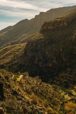 Uçsuz bucaksız bir yamaçtaki bir su değirmeninin engebeli kalıntısı, engebeli bir dağlık arazide biraz bitki örtüsü, mavi gökyüzünün altında biraz bulut. Nijar, Almerya, Endülüs, İspanya.