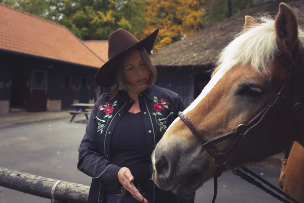 Žena s kloboukem krmení koní. — Stock fotografie