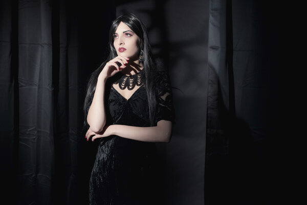 Dark mysterious witch fashion woman. Black curtains with window shadow on wall.