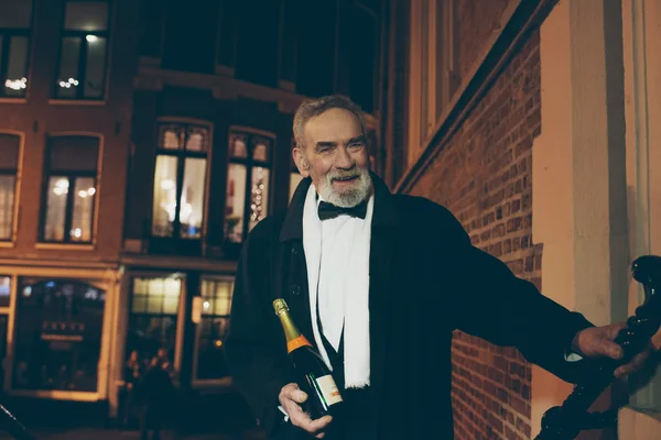 Smiling man in tuxedo with bottle — Stock Photo, Image