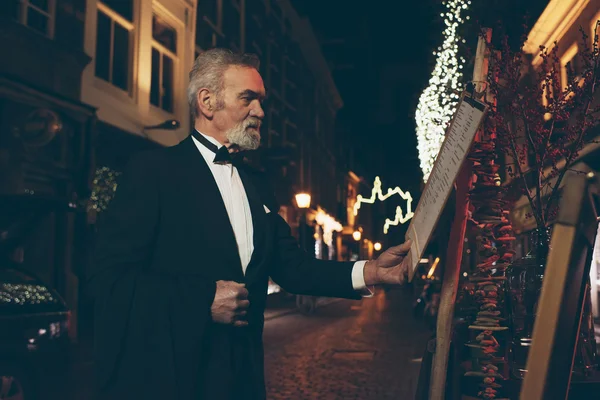 Man in tuxedo looking at menu of restaurant — Stock Photo, Image