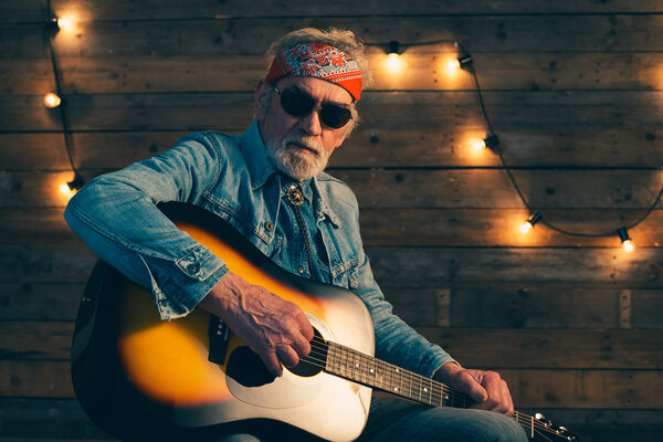 Senior guitarist with beard sitting on chair