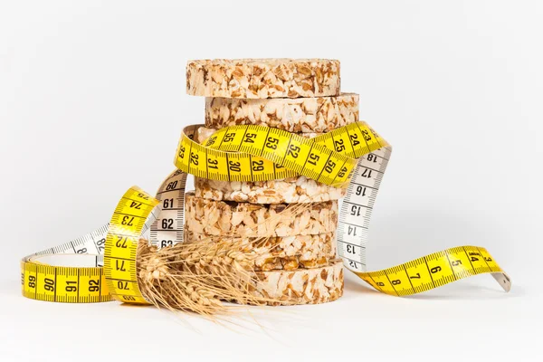Un nastro di misurazione giallo che avvolge un fascio di torte di grano e riso - concetto di alimentazione sana — Foto Stock