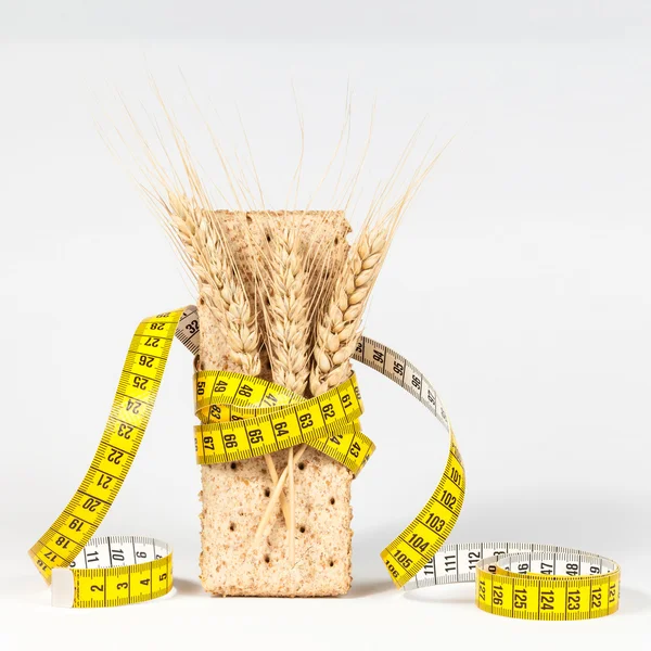 Una cinta métrica amarilla que envuelve la galleta de trigo o el pan crujiente y la gavilla de trigo - concepto de alimentación saludable —  Fotos de Stock