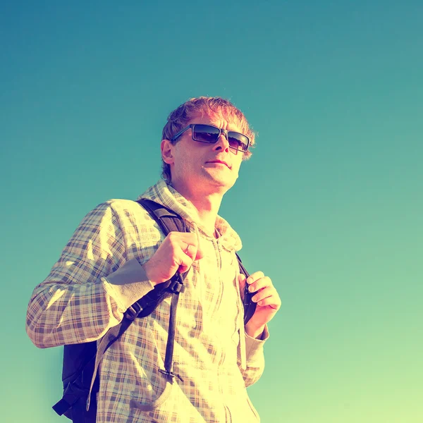 Stylized colorized vintage fashion portrait of happy man hiker holding backpack and looking at the sunset — Stock Photo, Image