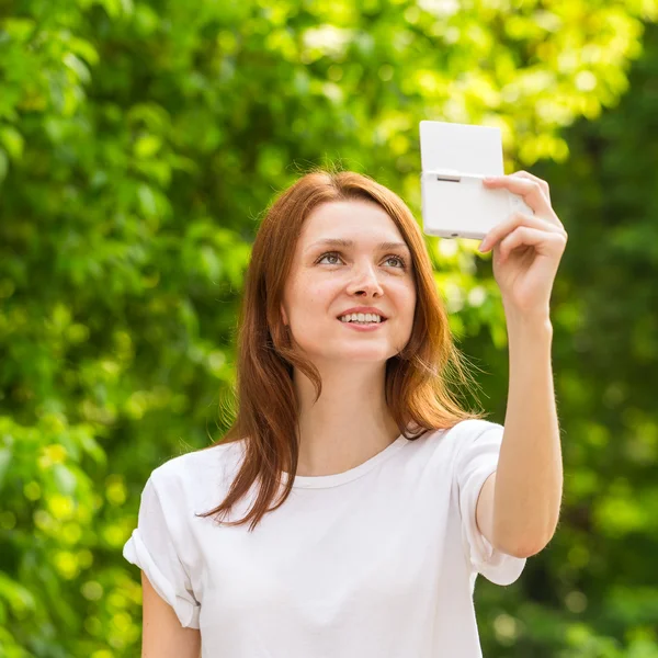 Beautiful young girl taking a selfie photo with beautiful bokeh on the background of green trees — Stock Photo, Image