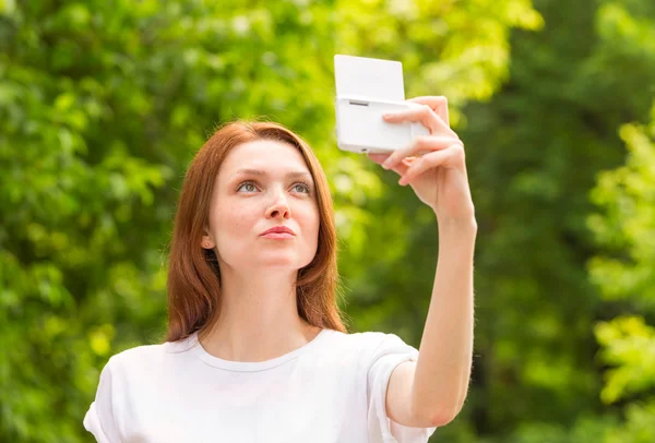 Beautiful young girl taking a selfie photo with beautiful bokeh on the background of green trees — Stock Photo, Image