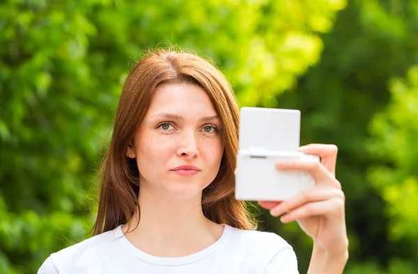 Beautiful young girl taking a selfie photo with beautiful bokeh on the background of green trees — Stock Photo, Image