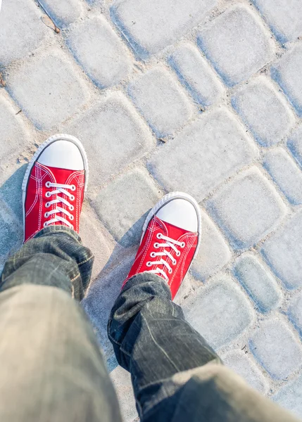 Arnavut kaldırımlı yolda kırmızı spor ayakkabı ayaklarda genç adam — Stok fotoğraf