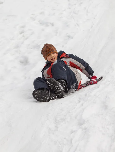 Divertimento invernale - slittino in inverno. Giovane ragazzo godendo di un giro in slitta in un bellissimo parco invernale innevato — Foto Stock