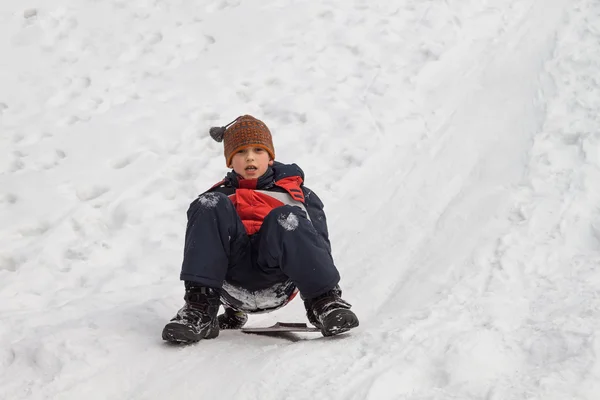 Divertimento invernale - slittino in inverno. Giovane ragazzo godendo di un giro in slitta in un bellissimo parco invernale innevato — Foto Stock