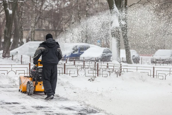 Kiev, Oekraïne - 09 januari 2016: Een man reinigt sneeuw van trottoirs met sneeuwblazer. — Stockfoto