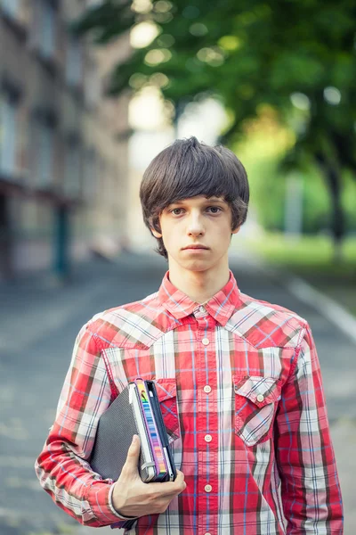 Jovem estudante segurando um livro e tablet contra um fundo da cidade — Fotografia de Stock