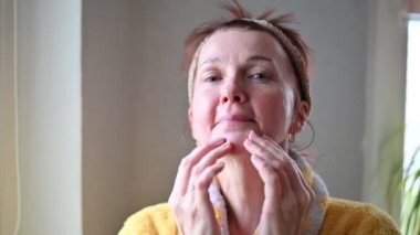 Portrait of 45 years old woman applying anti-aging cosmetics on her face at home