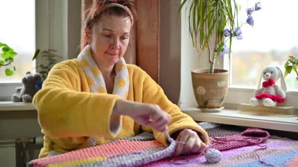 Portrait aged woman 45 years old at home hobby knits with her hands sitting at the table near the window — Stockvideo