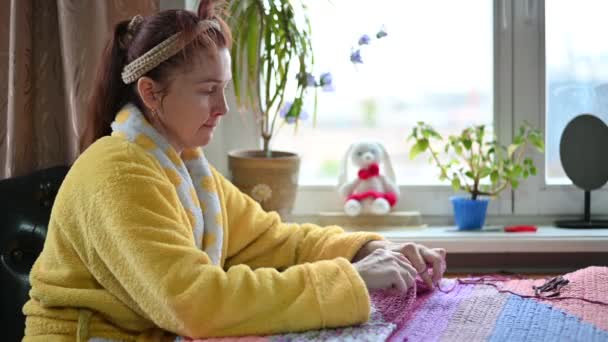 Portrait femme âgée 45 ans à la maison passe-temps tricot avec ses mains assises à la table près de la fenêtre — Video