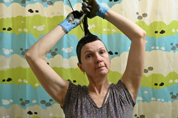 Portrait de femme brune caucasienne dans des gants seuls teint les cheveux. Le modèle se tient dans la salle de bain de la maison. — Photo