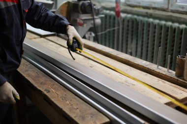 Bir işçinin fotoğrafı pencere pervazını şerit testereyle kesmek için bir mezura ile ölçer. Endüstriyel kavram.