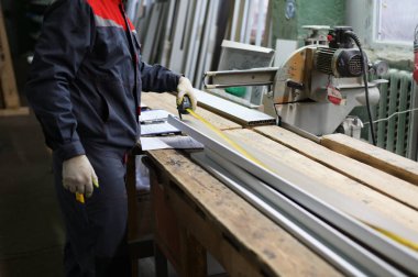 Bir işçinin fotoğrafı pencere pervazını şerit testereyle kesmek için bir mezura ile ölçer. Endüstriyel kavram.