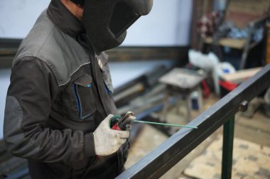 Bir kaynakçının bir atölyede metal bir masada maskeyle çalışırken fotoğrafı.