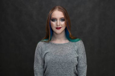 Saçları boyalı, parlak makyajlı ve gülümseyen beyaz bir kızın fotoğrafı..