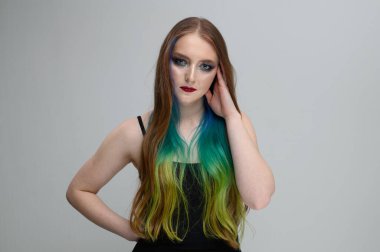 Beyaz arka planda parlak makyajlı ve boyalı saçları olan ciddi bir beyaz kızın portresi.