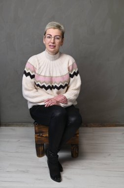 Saçları kısa saçlı, gri bir arka planda gülümseyen yetişkin, beyaz bir kadın.